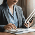 Une investisseuse en immobilier, vêtue d'un costume élégant, effectue un arbitrage bien locatif en analysant les rendements sur sa calculatrice tout en tenant son smartphone, avec une icône de maison et une flèche de croissance en superposition, symbolisant l'optimisation de son portefeuille immobilier