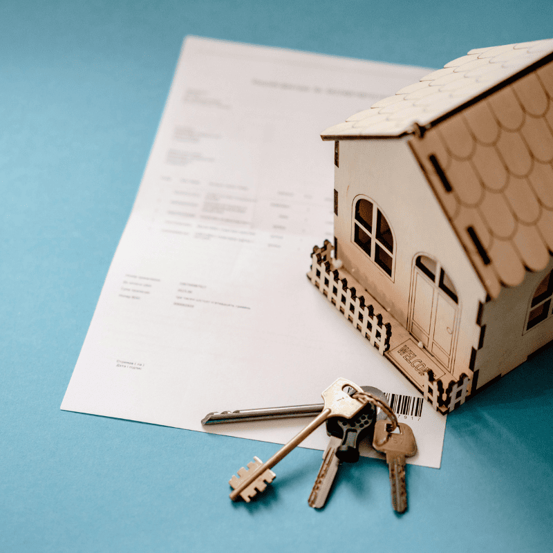 Maison miniature et ses clés posés sur une table bleu sur des documents symbolisant le prêt trésorerie hypothécaire suite à un refus de prêt immobilier classique.