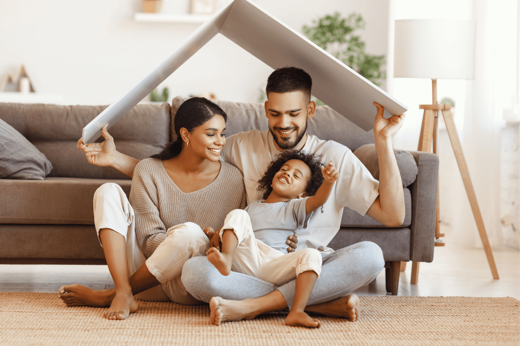 famille parents avec leur enfant, assis dans le salon portant le toit d'une petite maison au dessus de leurs têtes, symbolisant l'assurance